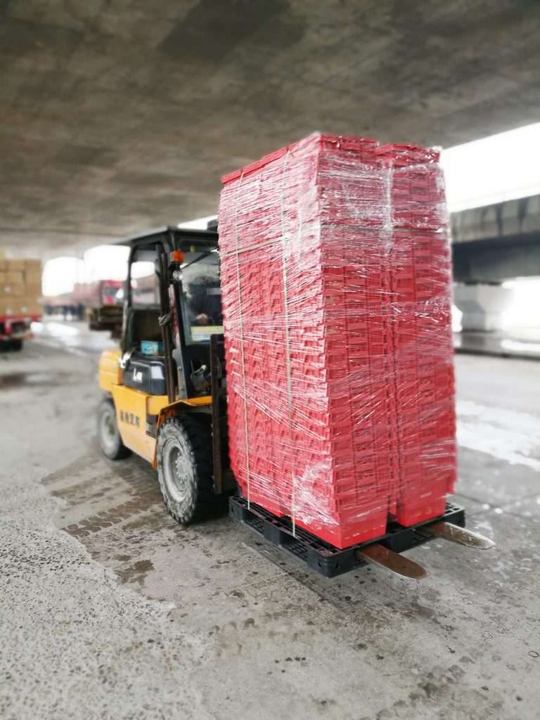 A fork lift a pallet which is full of nested red plastic moving boxes.