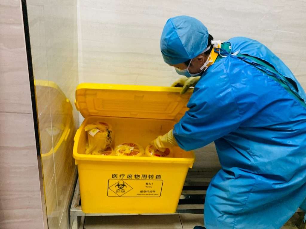 A doctor is throwing medical trash into a plastic crate.